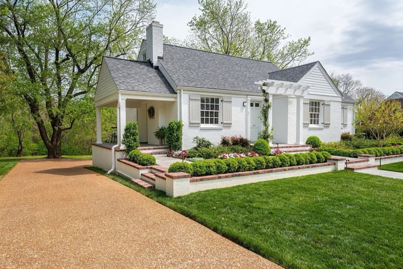 White brick Tennessee home with mature trees, landscaped gardens and a covered porch.